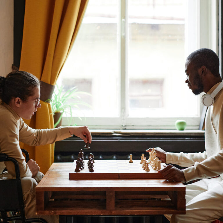 African man playing chess together with his friend with disability, they sitting in the room