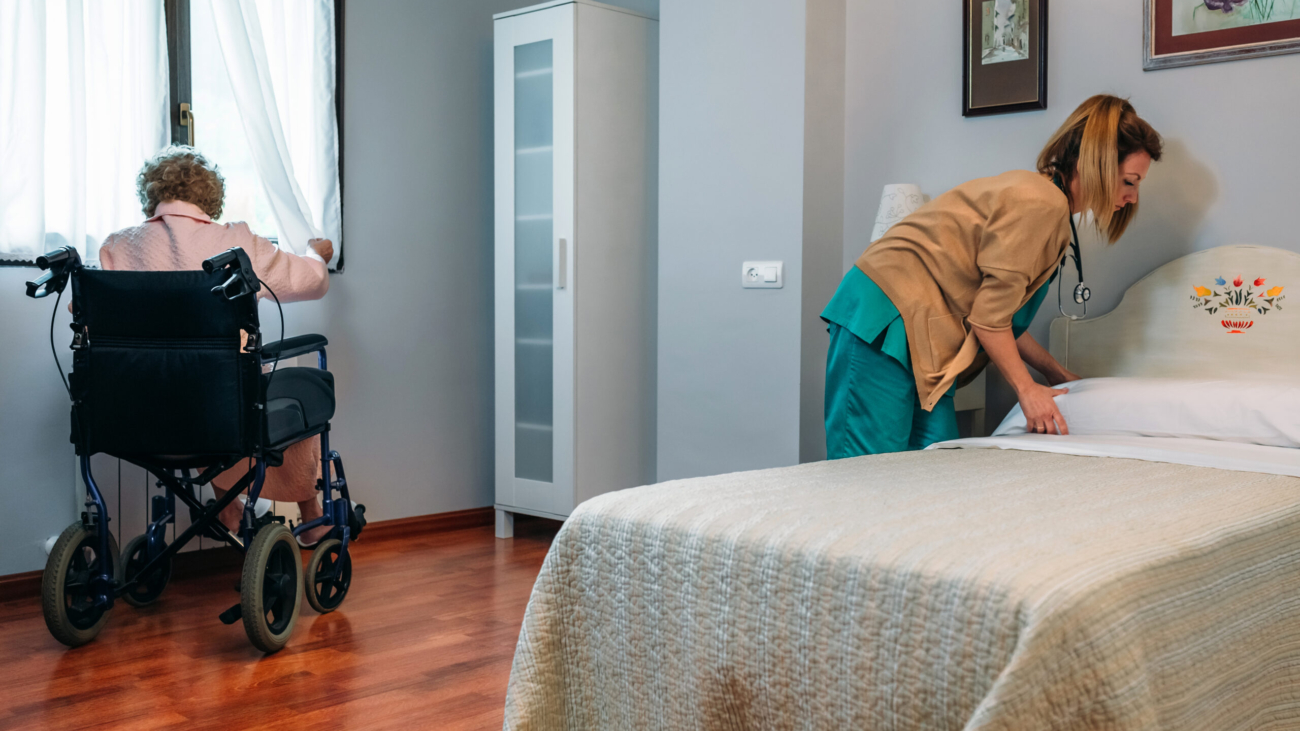 Caregiver making the bed of an elderly patient in a nursing home