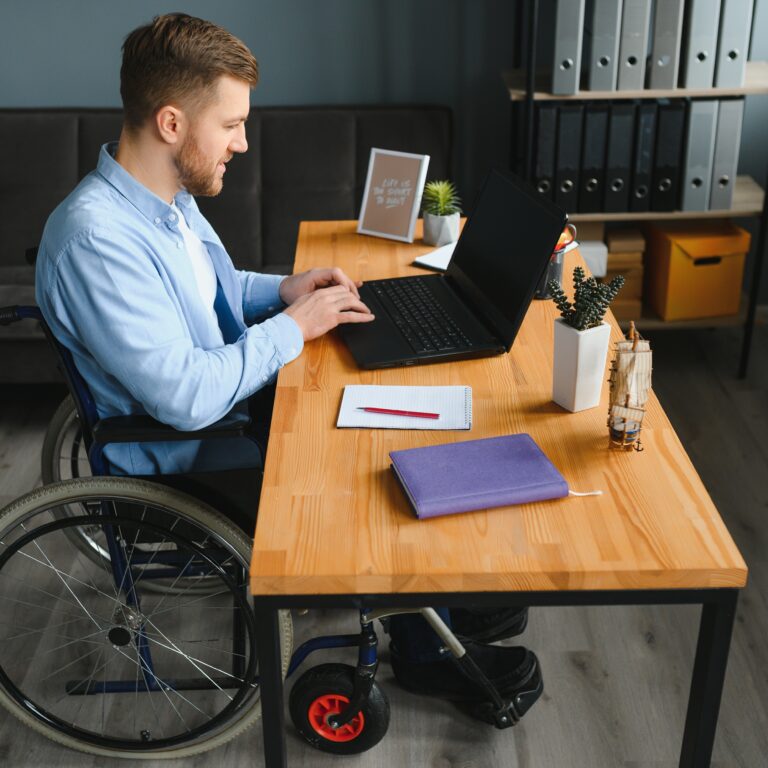 Handicapped Businessman Sitting On Wheelchair And Using Computer In Office