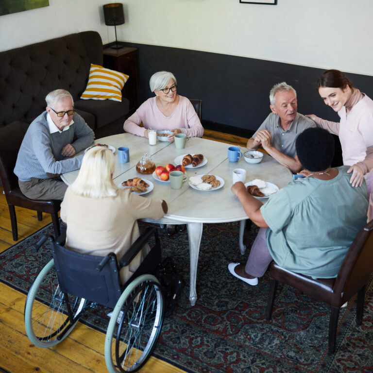 High angle view at diverse group of senior people enjoying breakfast at dining table in nursing home, copy space